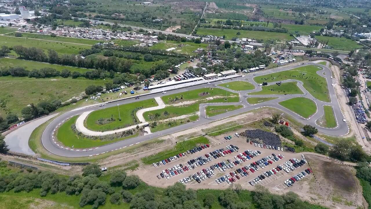 Luftfoto af et baneanlæg med grønne arealer mellem banerne og en fyldt parkeringsplads.