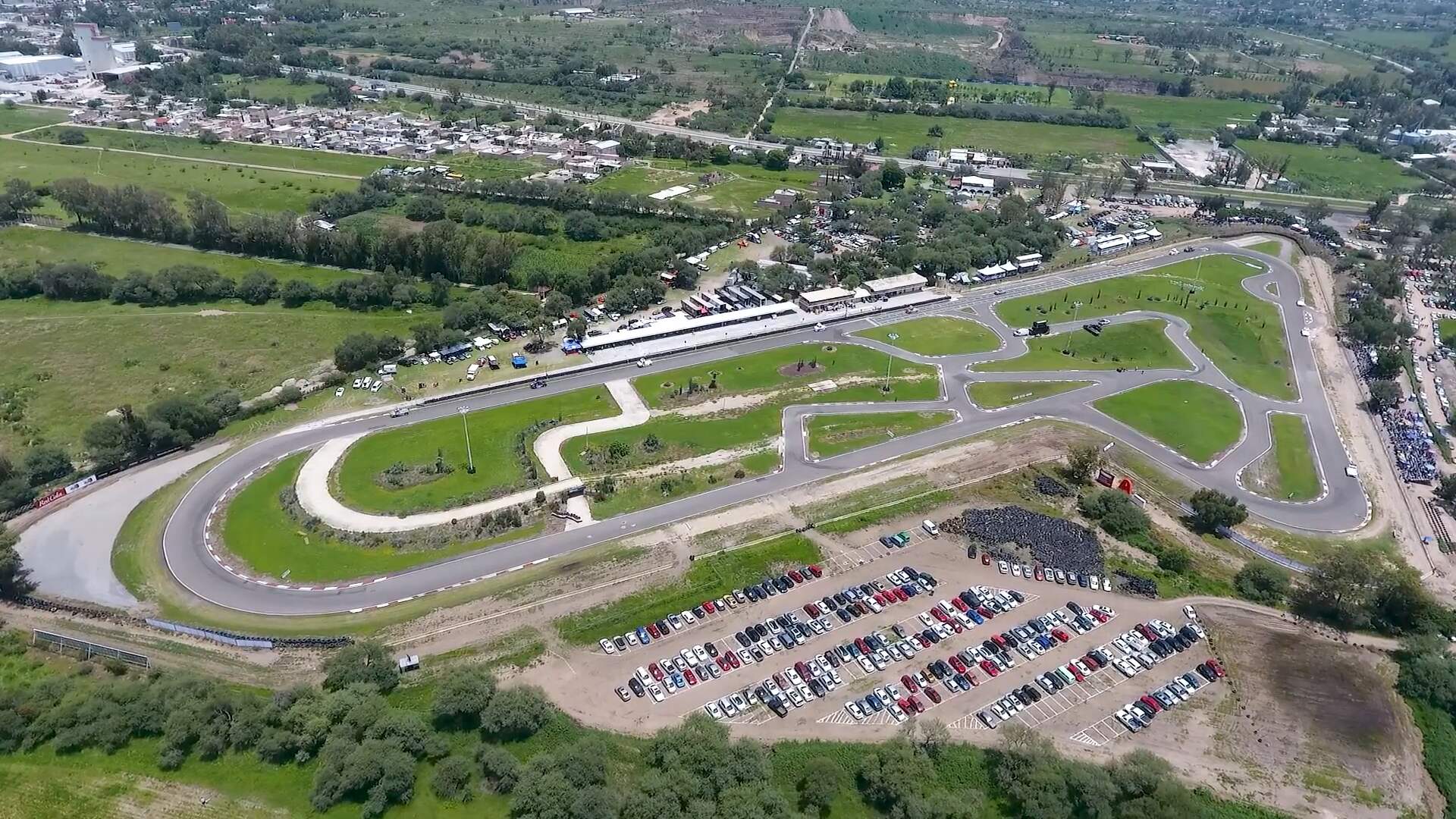 Luftfoto af et baneanlæg med grønne arealer mellem banerne og en fyldt parkeringsplads.