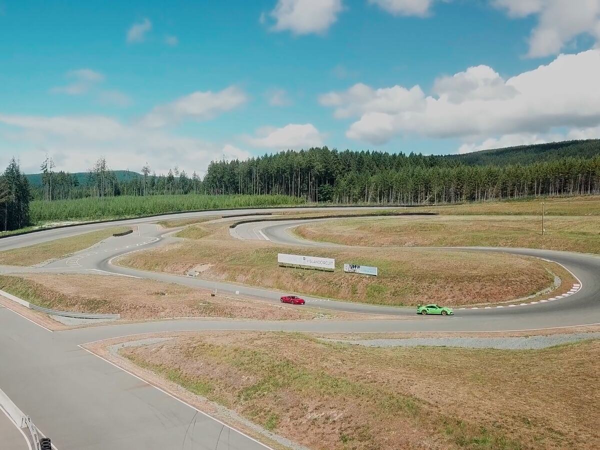 Biler på en snoet øvelsesbane i solskin med skov i baggrunden.